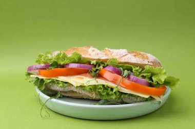 Delicious ciabatta sandwich with prosciutto, cheese and vegetables on green background, closeup
