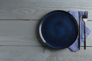 Clean ceramic plate, cutlery and napkin on grey wooden table, flat lay. Space for text