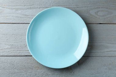 Gri ahşap masadaki temiz seramik tabak, üst manzara.