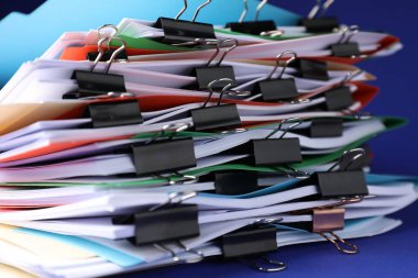 Many folders with documents and binder clips on blue background, closeup