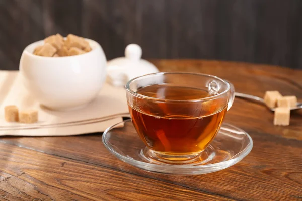 Cam bardakta koyu siyah çay ve ahşap masada kahverengi şeker, yakın plan.