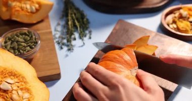 Açık mavi arka planda balkabağı kesen kadın, yakın plan.