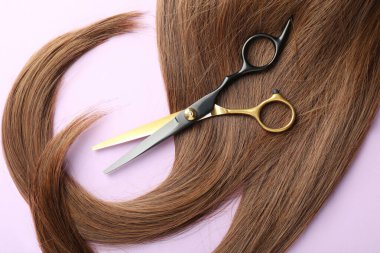 Açık mor zemin üzerinde güzel kahverengi saç ve makas, üst görünüm