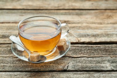 Aromatic black tea in glass cup, brown sugar and spoon on wooden table, closeup. Space for text