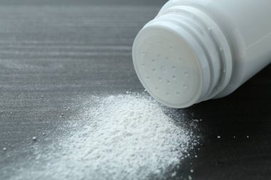 Container with talcum powder on black wooden table, closeup. Space for text