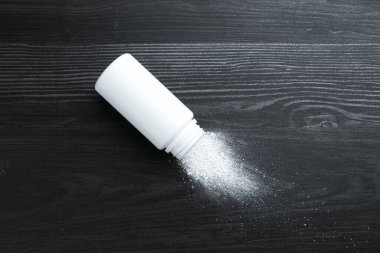 Container with talcum powder on black wooden table, top view. Space for text