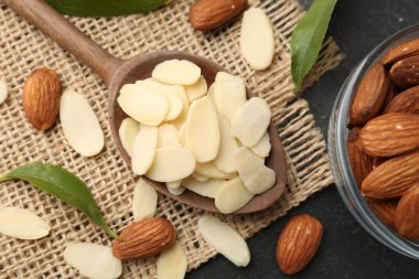 Fresh almond flakes, whole nuts and green leaves on grey table, above view