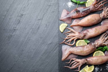 Raw squids, lemon and basil on black table, top view. Space for text