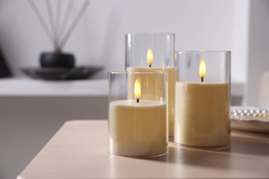 Decorative LED candles on wooden table at home, closeup. Space for text