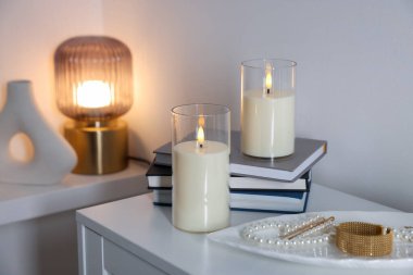 Beyaz dolaptaki dekoratif LED mumlar, kitaplar ve inci mücevherler.