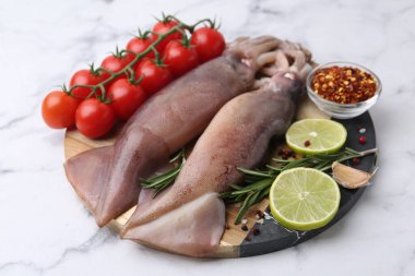 Fresh raw squids, tomatoes, lime slices and spices on white marble table, closeup