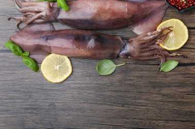 Raw squids, lemon slices, spices and basil on wooden table, flat lay. Space for text