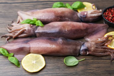 Raw squids, lemon slices, spices and basil on wooden table, closeup
