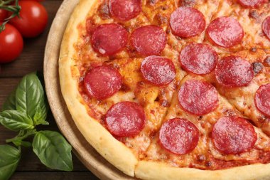 Lezzetli biberli pizza, taze domates ve ahşap masada fesleğen, yakın plan.