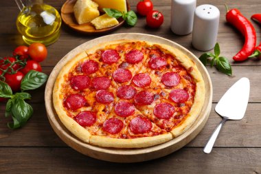 Lezzetli biberli pizza, servis elemanı ve ahşap masadaki malzemeler.