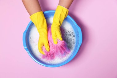 Kadın elbiselerini pembe arka planda plastik bir leğenle yıkıyor.