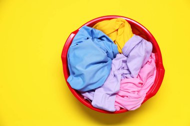 Plastic basin with clothes on yellow background, top view