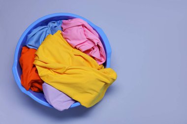 Plastic basin with clothes on light purple background, top view. Space for text