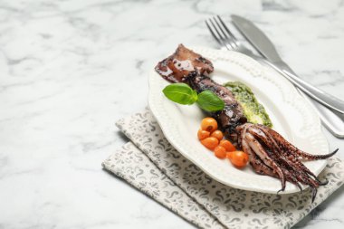 Soslu, domatesli, çatal bıçaklı ve fesleğenli kalamar, beyaz mermer masa, yakın çekim. Metin için boşluk