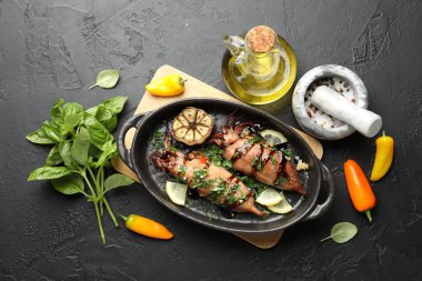 Tasty cooked squids with sauce, garlic and products on black table, flat lay