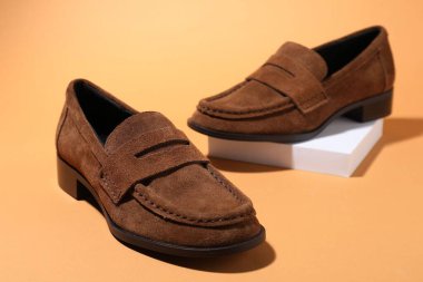 Soluk turuncu arka planda bir çift şık kahverengi ayakkabı, yakın plan.