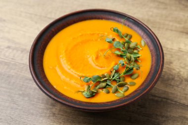 Delicious pumpkin soup with seeds and microgreens in bowl on wooden table, closeup