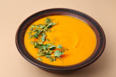 Çekirdekli lezzetli balkabağı çorbası ve bej masadaki mikro yeşiller, yakın plan.