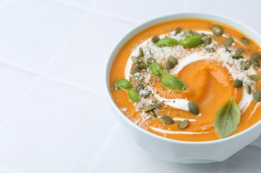 Delicious pumpkin soup with spices, cheese and sour cream in bowl on white tiled table, closeup. Space for text