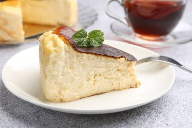 Piece of delicious Basque cheesecake with mint and tea on light grey table, closeup