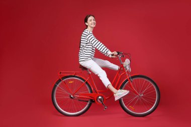 Kırmızı arka planda bisiklet süren gülümseyen kadın. Metin için boşluk