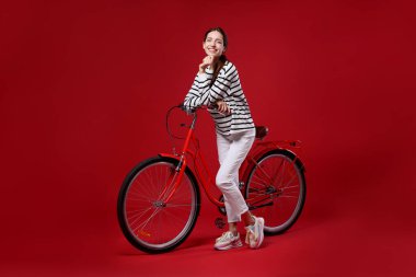 Kırmızı arka planda bisiklet süren gülümseyen kadın.