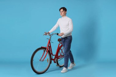 Açık mavi arka planda kırmızı bisikletli yakışıklı bir adam.
