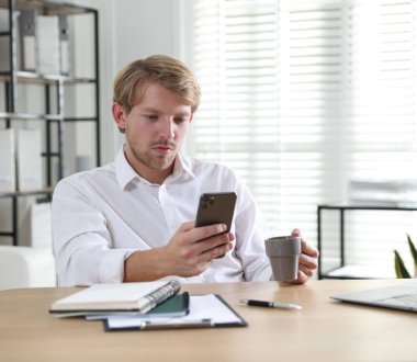 İçkili bir adam ahşap masada akıllı telefon kullanıyor.