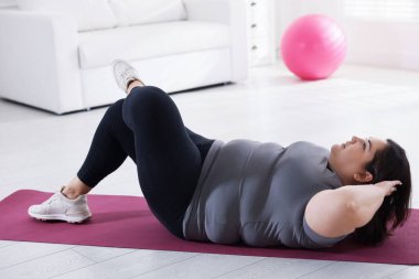 Evde yoga minderinde spor giyim eğitimi alan kilolu bir kadın.