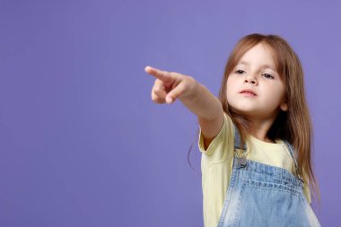 Tulum giymiş şirin küçük kız menekşe arkaplanındaki bir şeyi işaret ediyor. Metin için boşluk