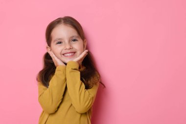 Pembe arka planda gülümseyen küçük bir kızın portresi. Metin için boşluk