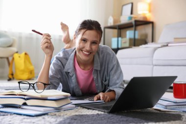 Bilgisayarlı, kitaplı ve kalemli gülümseyen bir öğrenci içeride sınava hazırlanıyor.