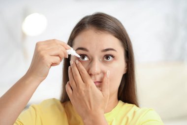 Evde göz damlası süren genç bir kadın.