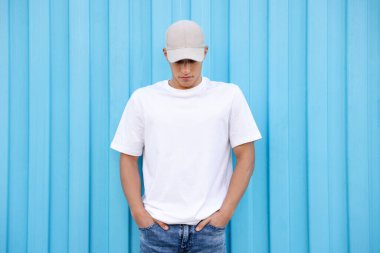 Açık mavi duvarın yanında beyaz tişört giyen genç bir adam. Tasarım için model