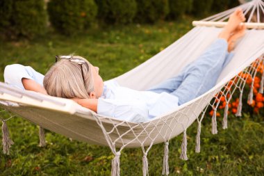 Dışarıda rahat bir hamakta dinlenen yaşlı kadın.