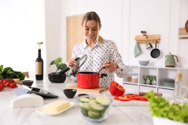 Mutfaktaki masada yemek yapan gülümseyen kadın.