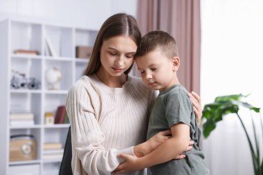 Anne, üzgün oğlunu evde destekleyip kucaklıyor.