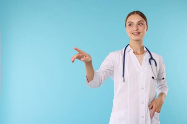 Steteskoplu profesyonel hemşire açık mavi arka planda bir şeyi işaret ediyor.