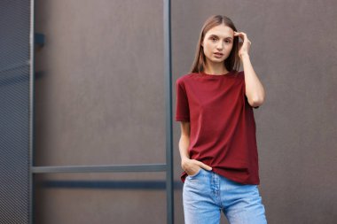 Gri duvarın yanında kırmızı tişört giyen genç bir kadın. Tasarım için model