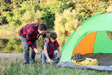 Baba ve oğul nehir kenarında kamp çadırı kuruyorlar.