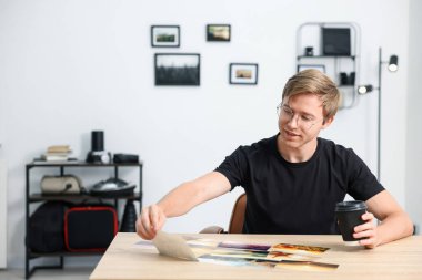 Kağıt bardakta içki içen profesyonel fotoğrafçı stüdyodaki ahşap masada çalışıyor.