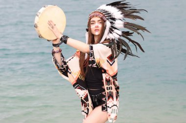 Kızılderili başlıklı güzel bir şaman kadın. Yüzü boyalı ve tef çalıyor. Nehir kenarında ayin yapıyor.