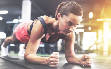 Atletik kadın spor salonunda yoga minderi üzerinde kalas egzersizi yapıyor.