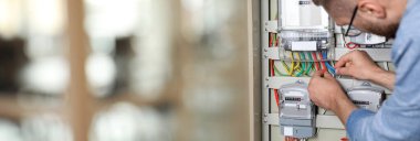 İçerideki elektrik sayacındaki kabloları kontrol eden adam, yakın plan. Pankart tasarımı