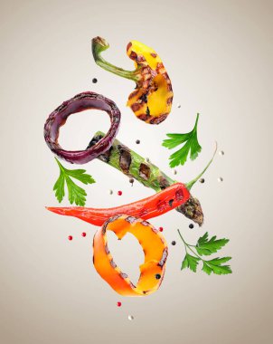 Grilled vegetables, parsley and peppercorns falling on grey gradient background